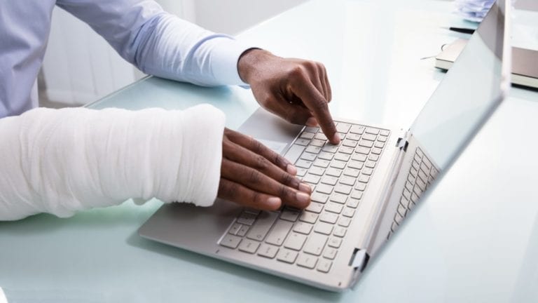 Person with an injured arm typing on a laptop