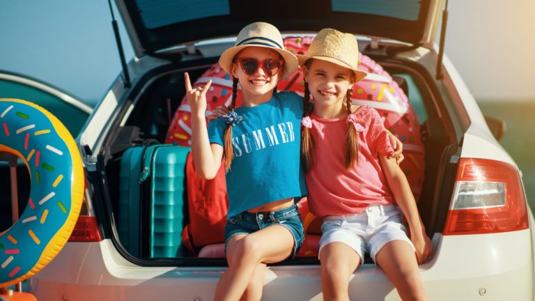 two young girls sitting on the trunk of a car before a summer road trip