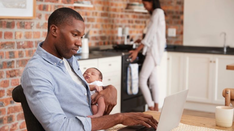 african american man holding baby while researching on his laptop