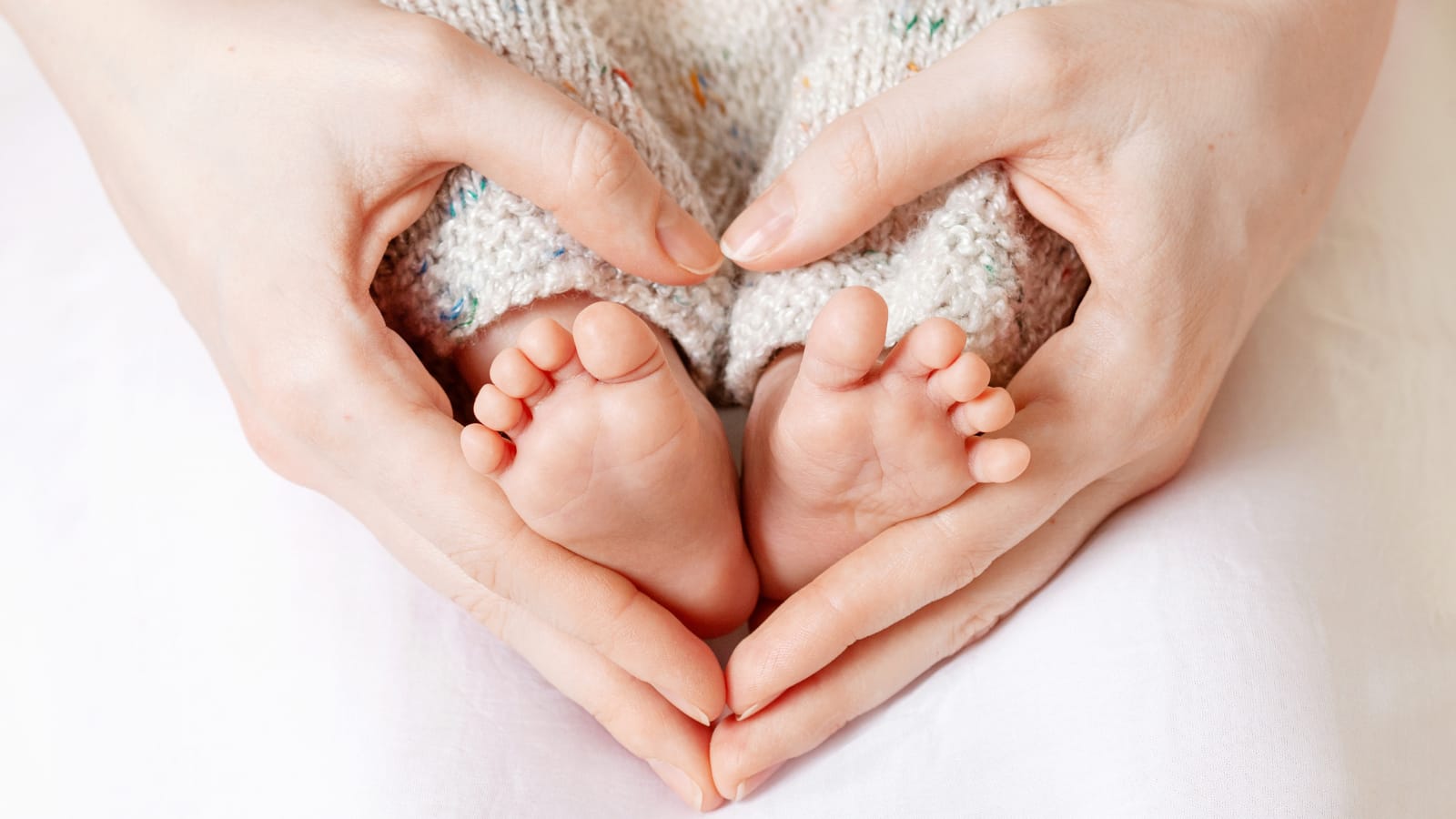 A mother's hands in the shape of a heart holding her newborn's feet
