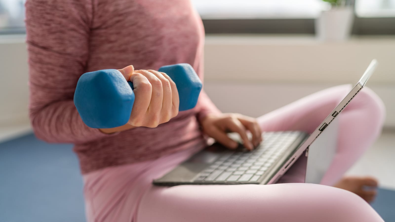 Woman working on laptop with one hand and holding a dumbbell with the other
