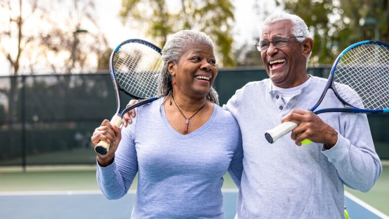 senior couple walking off the tennis court with rackets