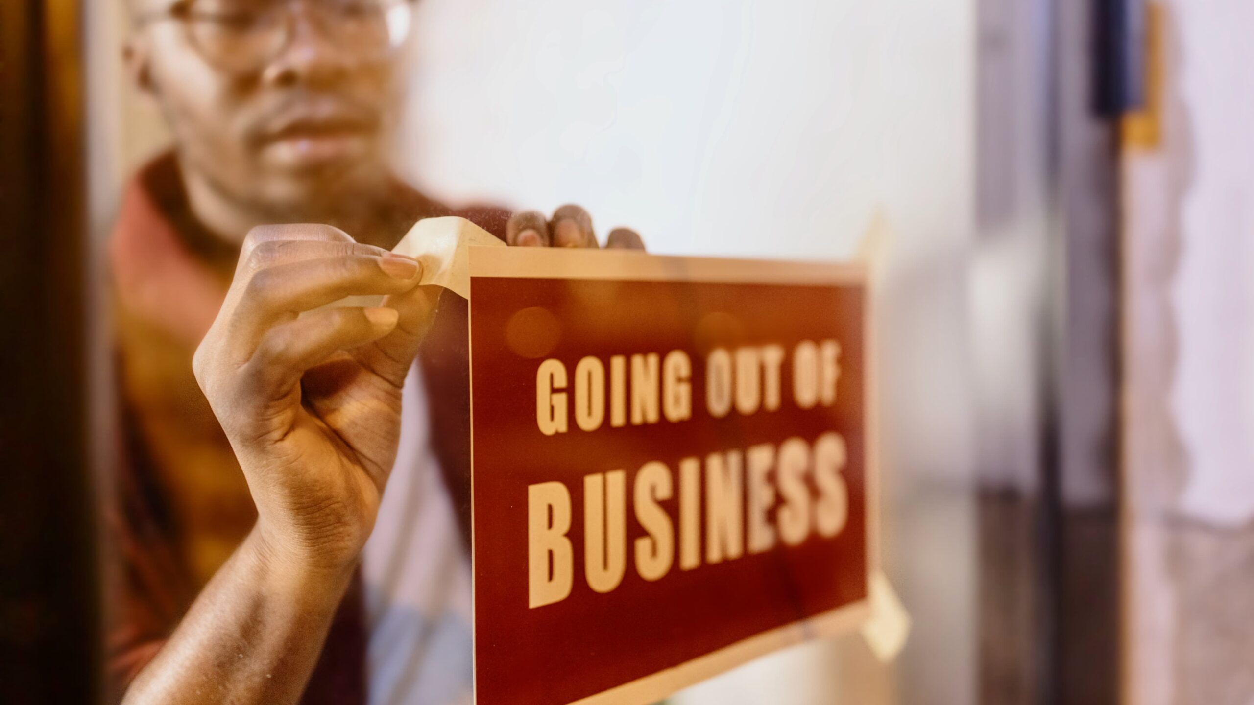 African-American business owner putting up a sign in the window saying "going out of business"