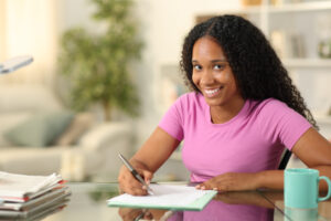 Happy young black woman filling out a form looks at you