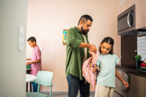 Father helps daughter put on a backpack.