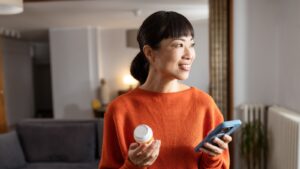 Asian woman on phone smiling holding prescription bottle